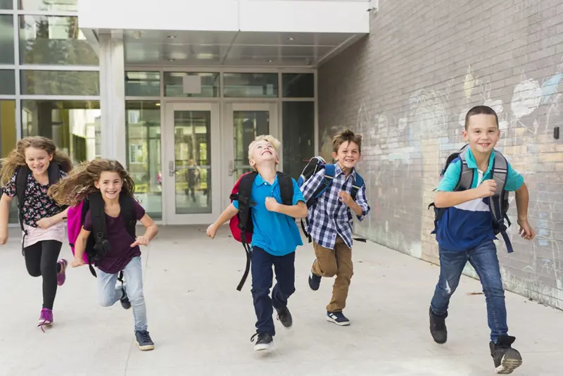 Glade skoleelever som løper med skolesekker