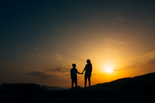 Silhuett av en mor og et barn som holder hender i en solnedgang