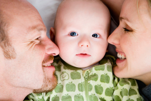 en baby ligger mellom en smilende mor og far