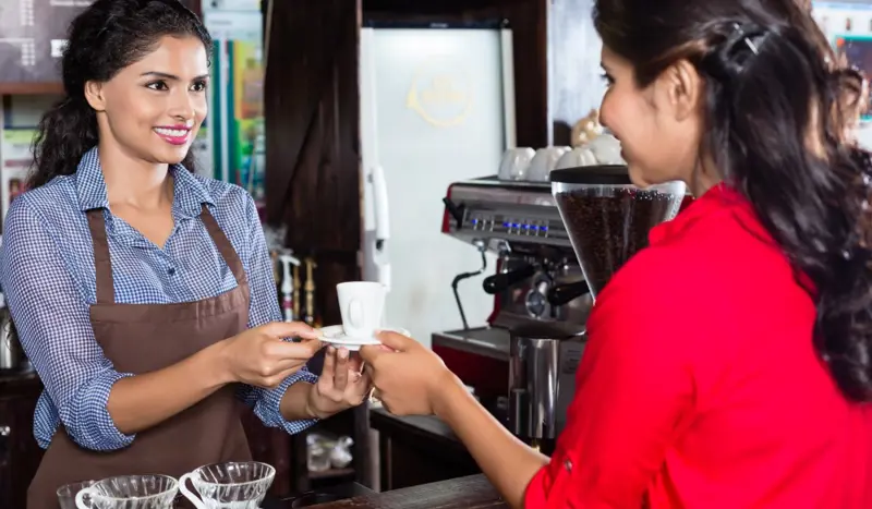 Kvinnelig servitør serverer kaffe til kvinnelig kunde ved disken