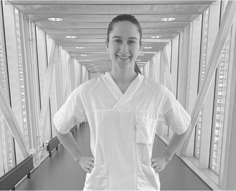 Kvinnelig sykepleier i hvit uniform som står med hendene i siden. Uniformsermene rekker ned til albuen. Illustrerer hva det vil si å være bar fra albuen og ned.