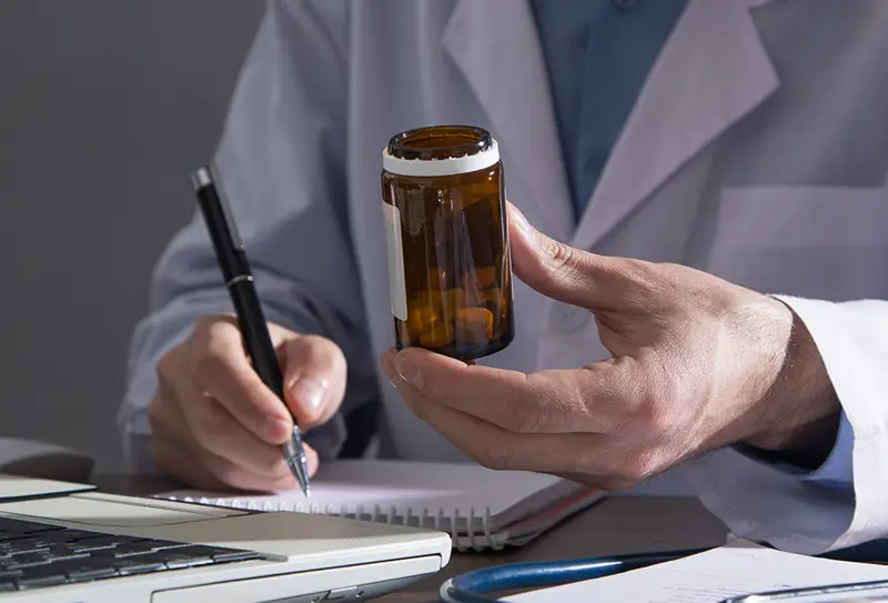 Lege foran pc med pilleglass og penn i hendene. Bilde.