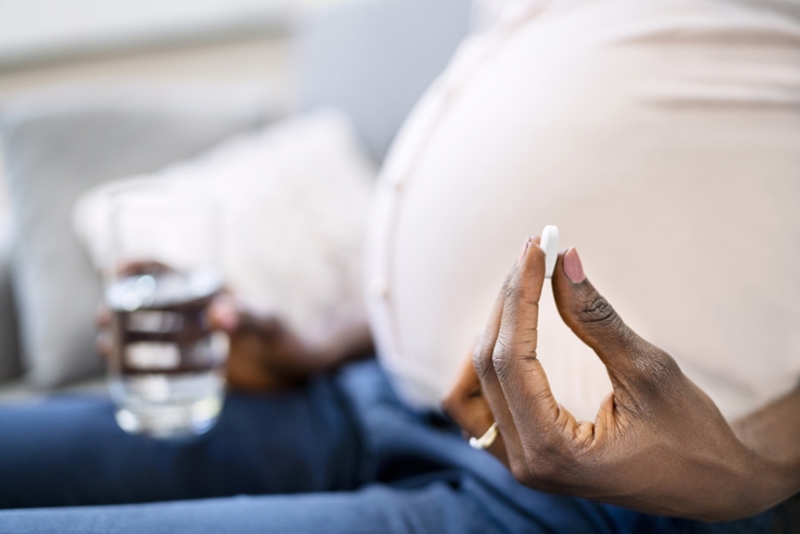 Gravid afrikansk kvinne som holder en pille i hånden