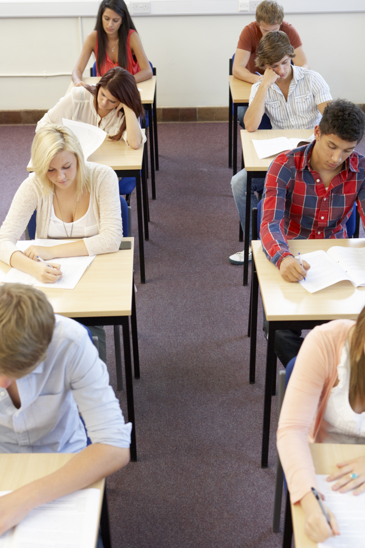 Elever som sitter på rad på stoler og besvarer eksamen på papir