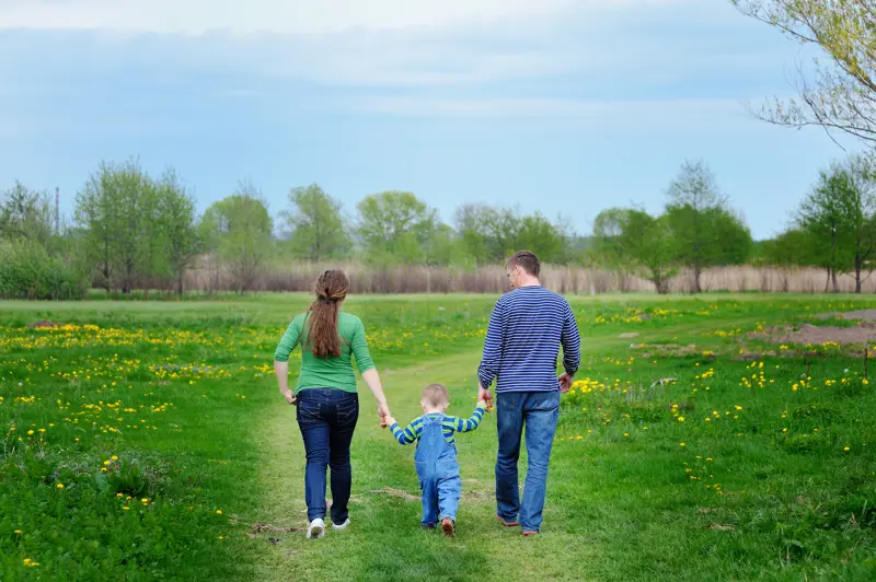 Foreldre og et lite barn holder hender ute på grønn eng