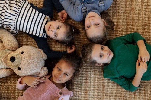 Bilde av barn som smiler, ligger på gulvet og ser opp mot kamera