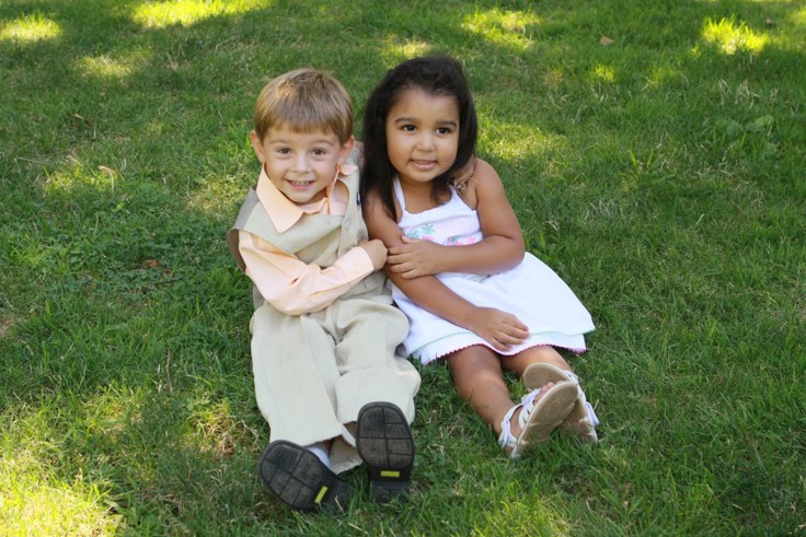 To små barn sitter ved siden av hverandre i gresset og holder rundt hverandre