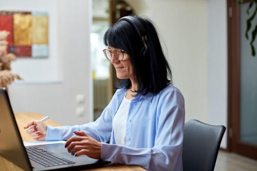 Mørkhåret kvinne som sitter med headset og briller og skriver på en PC, hun er deltaker på et webinar