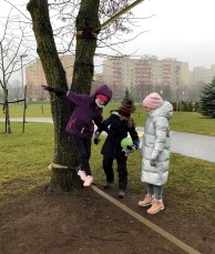 Tre barn øver seg på slakk line festet mellom to trær