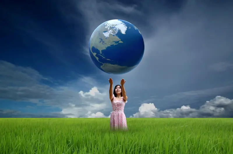 Person standing on a field holding up the globe in its hands